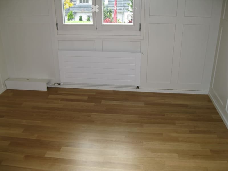 Empty room with wooden flooring, white walls, and a radiator under a window.