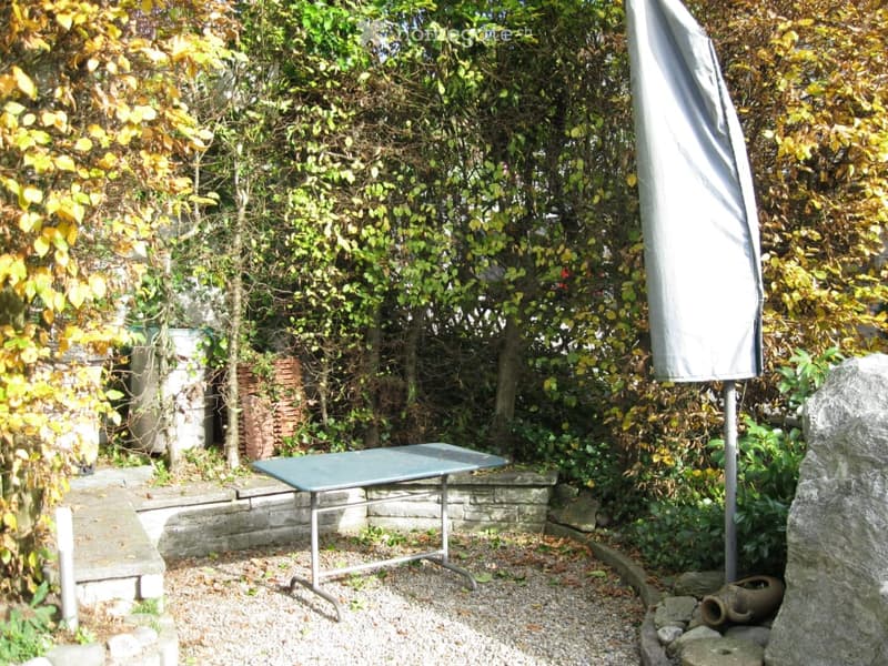 A small outdoor garden area with a metal table, umbrella, and surrounding greenery.