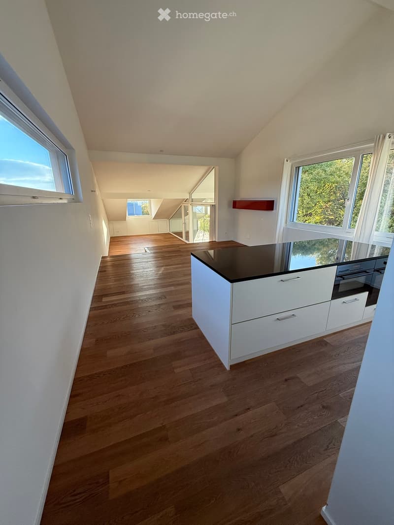 Bright, open kitchen with wooden flooring, white cabinets, and large windows offering natural light and a view of greenery.