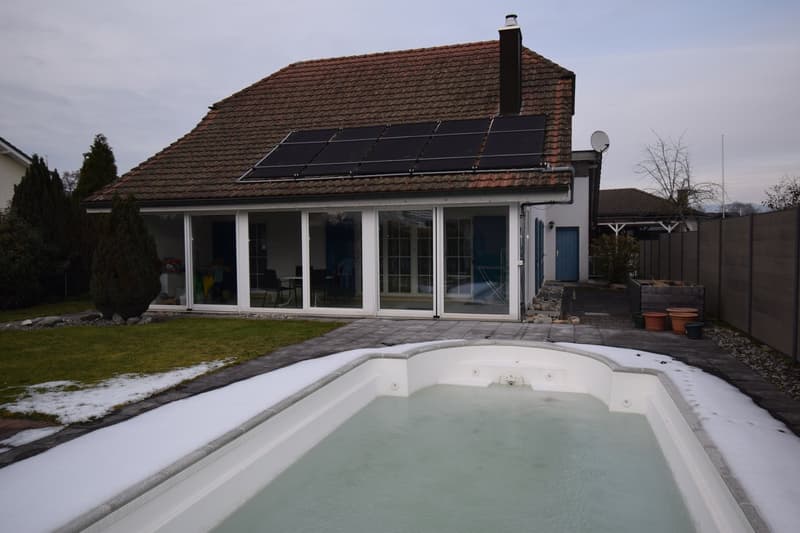 Red tiled roof, solar panels, large glass windows, rectangular pool with snow