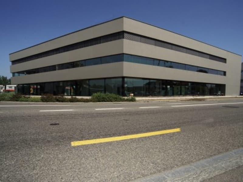 Modern office building, three stories, glass windows, concrete structure, parking lot in front