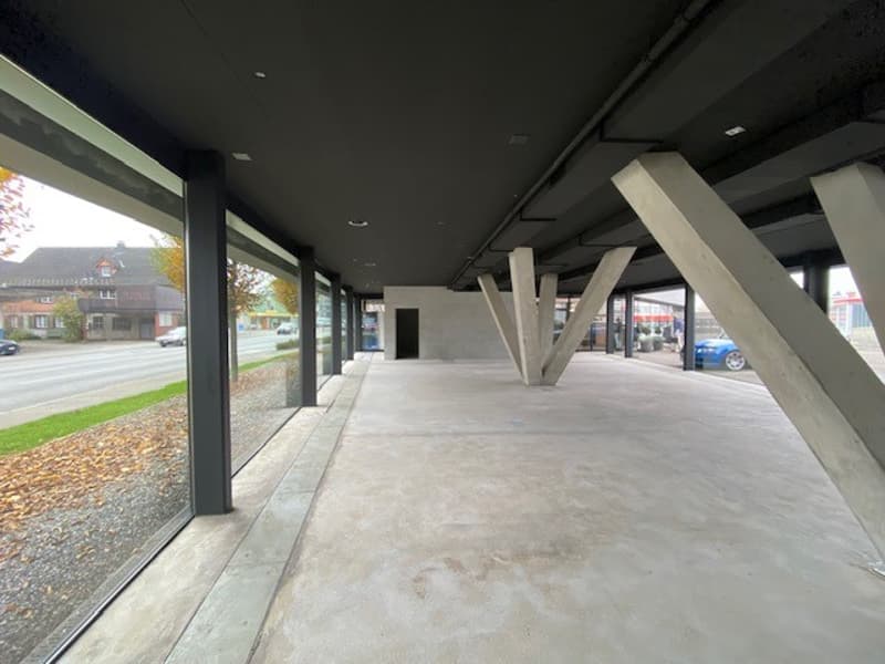 large empty concrete floor, glass walls, beams on ceiling, outside