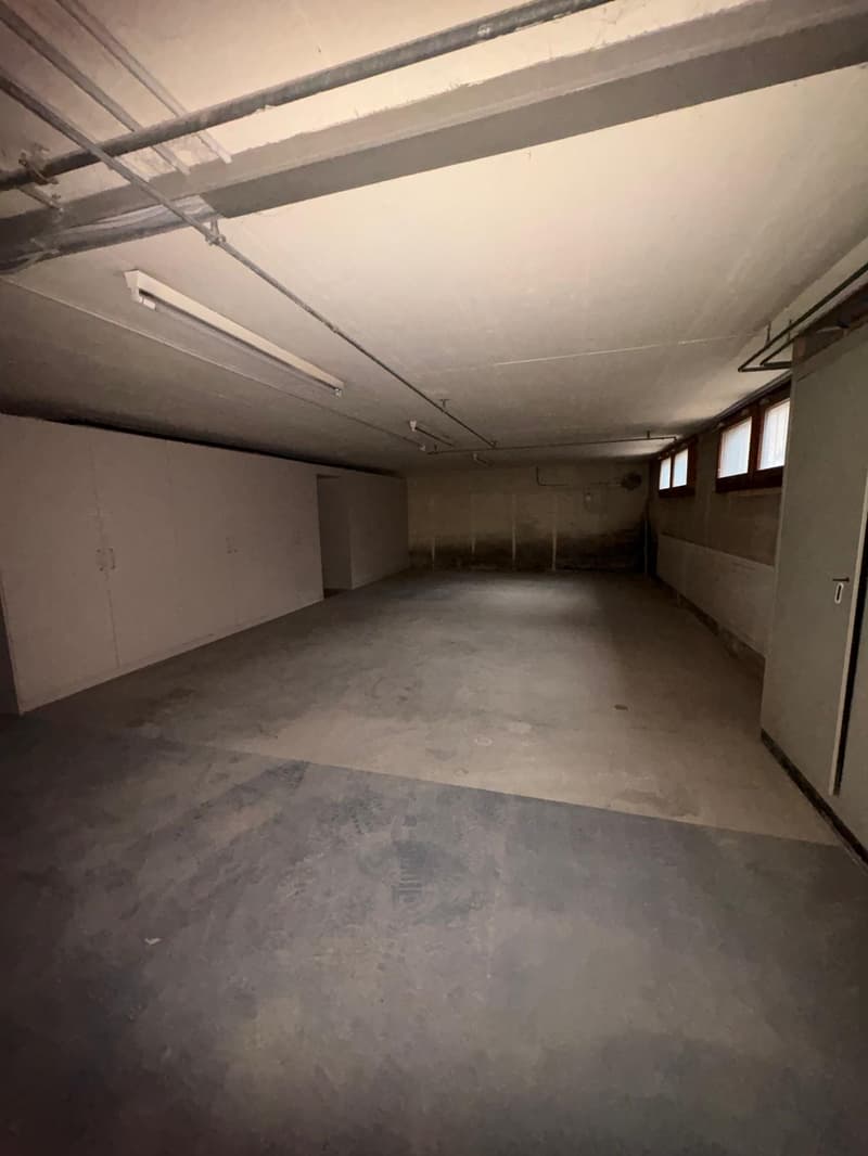 A storage room with concrete floor, metal ceiling beams, white walls, three windows, and two long wall cabinets.