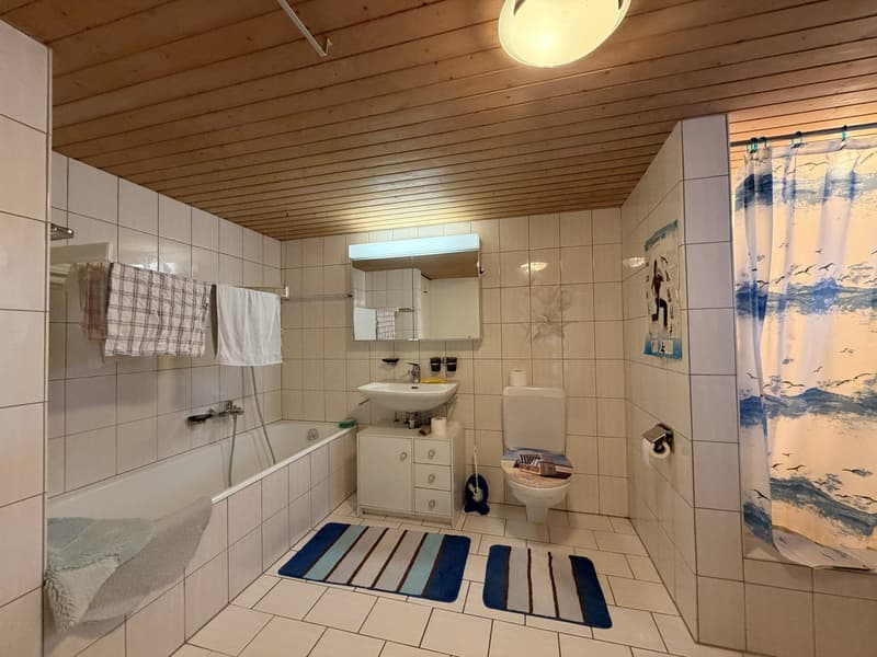 Bathroom with bathtub, toilet, sink, wooden ceiling, white tiles, towels, and a shower curtain