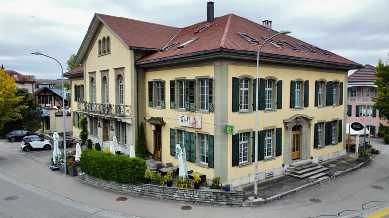 2 story yellow house, red roof, green shutters, balcony, plants, cars parked