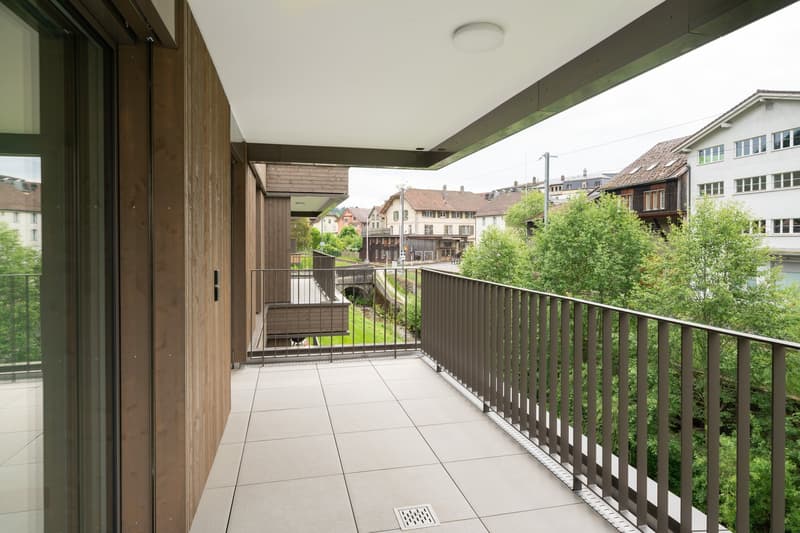 Spacious balcony with wooden walls, metal railing, and a view of the surrounding buildings and greenery