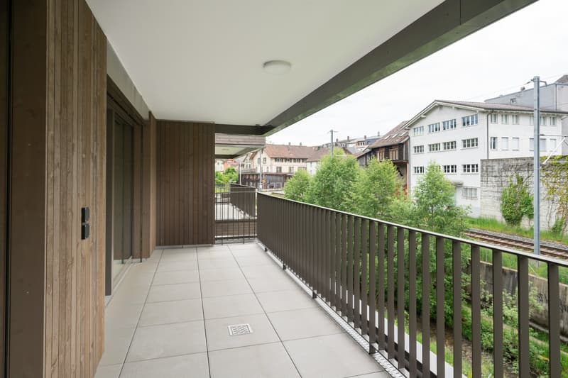 Spacious balcony with wooden walls, metal railing, and a view of the surrounding buildings and greenery.