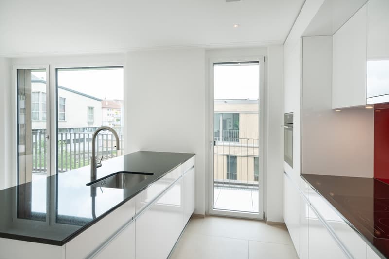 Spacious kitchen with modern white cabinets, black countertop, stainless steel sink, and large windows overlooking a balcony or terrace