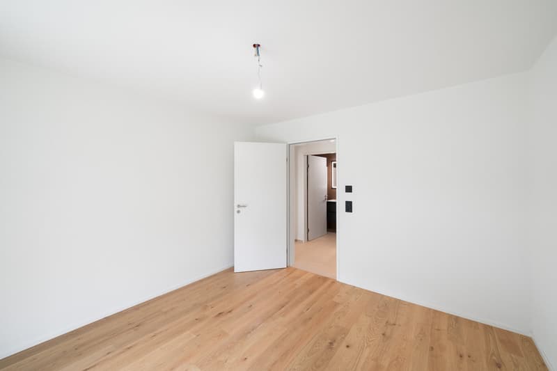 Empty room with white walls, hardwood flooring, and a white door leading to another room.