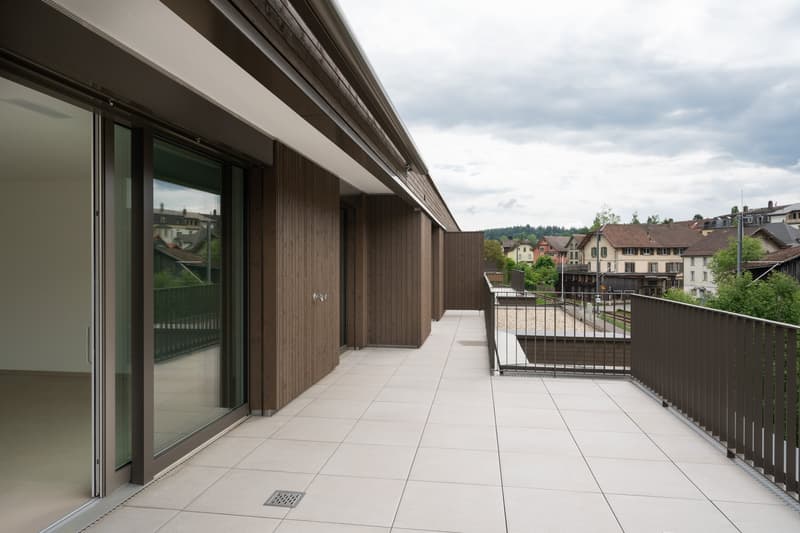 Spacious balcony with wooden siding, large sliding glass doors, tiled flooring, overlooking a residential neighborhood with houses and trees