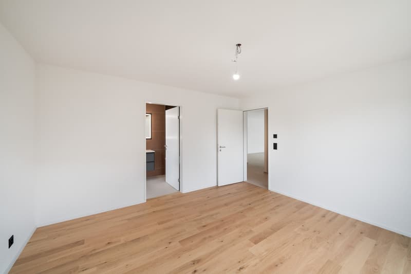 Empty room with white walls, hardwood flooring, and two doors leading to other rooms or areas.