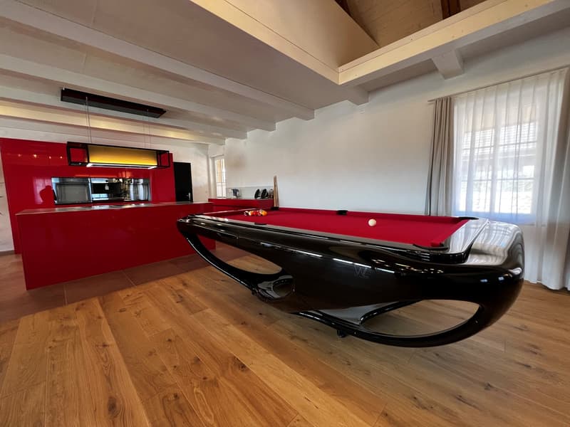 Spacious game room with a black and red pool table, hardwood floors, and a modern kitchen with a dishwasher visible in the background.