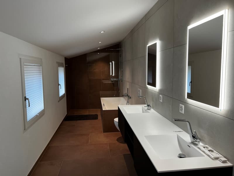 Large modern bathroom with gray tile walls, double vanity with white countertop, recessed lighting, and a separate shower area