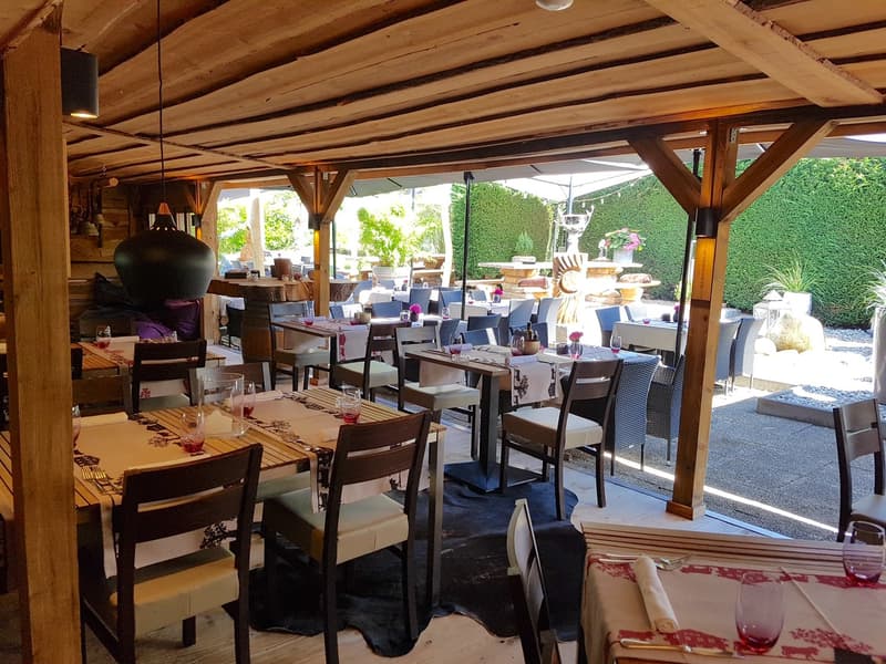 Rustic wooden beamed ceiling, outdoor seating area with tables and chairs, potted plants and decor, large windows overlooking a garden area