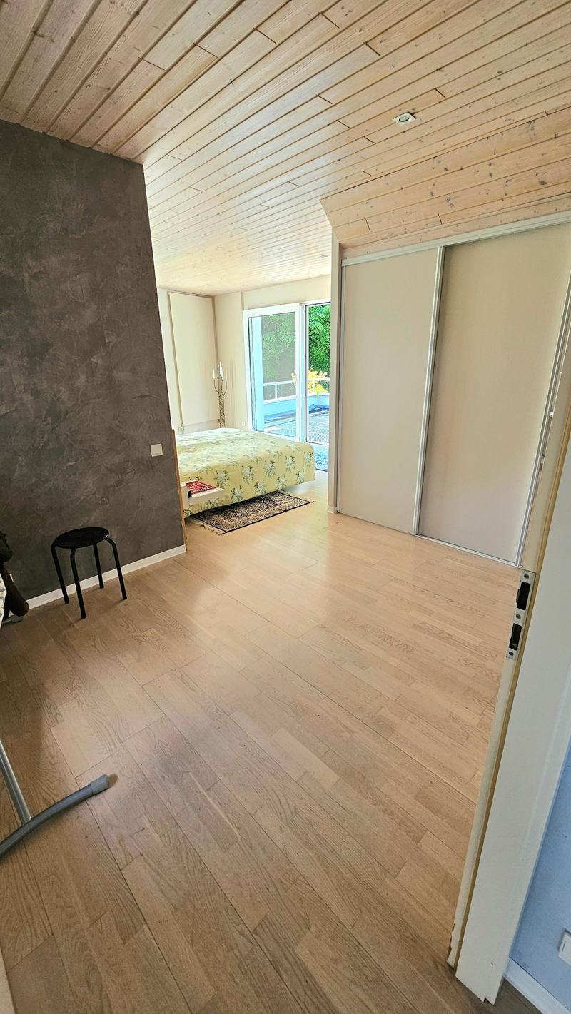 Spacious bedroom with wooden ceiling, hardwood floors, sliding glass doors leading to a balcony or terrace, and a floral-patterned bed.