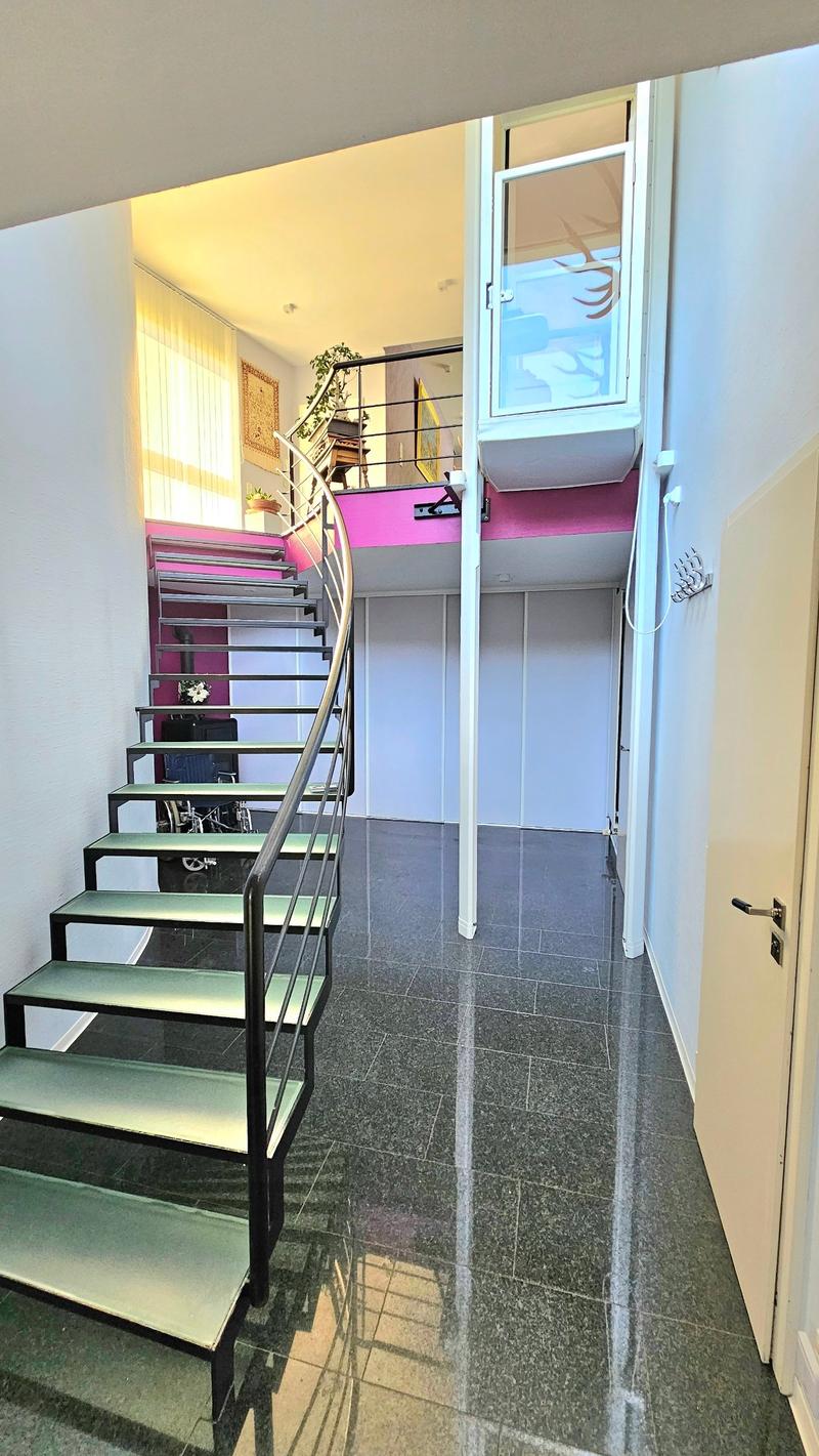Spiral staircase leading to a loft or upper level, with a window providing natural light. The floor is tiled with a granite or stone-like material. The space appears to be a modern, open-concept apartment or studio unit.