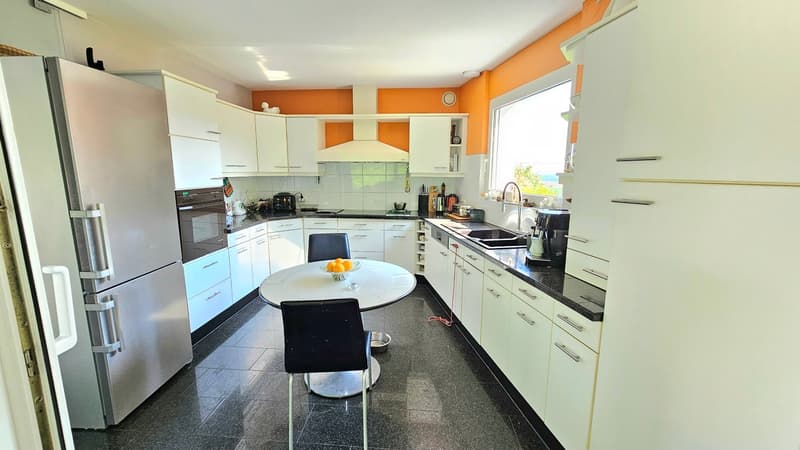 Spacious kitchen with white cabinets, black granite countertops, stainless steel appliances including a refrigerator and dishwasher, and a round dining table with chairs.