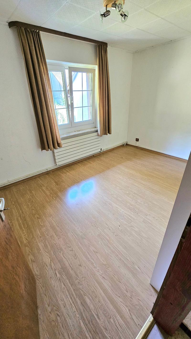 hardwood floor, white walls, large window with curtain, radiator below window, spotlights on ceiling, power outlet on wall
