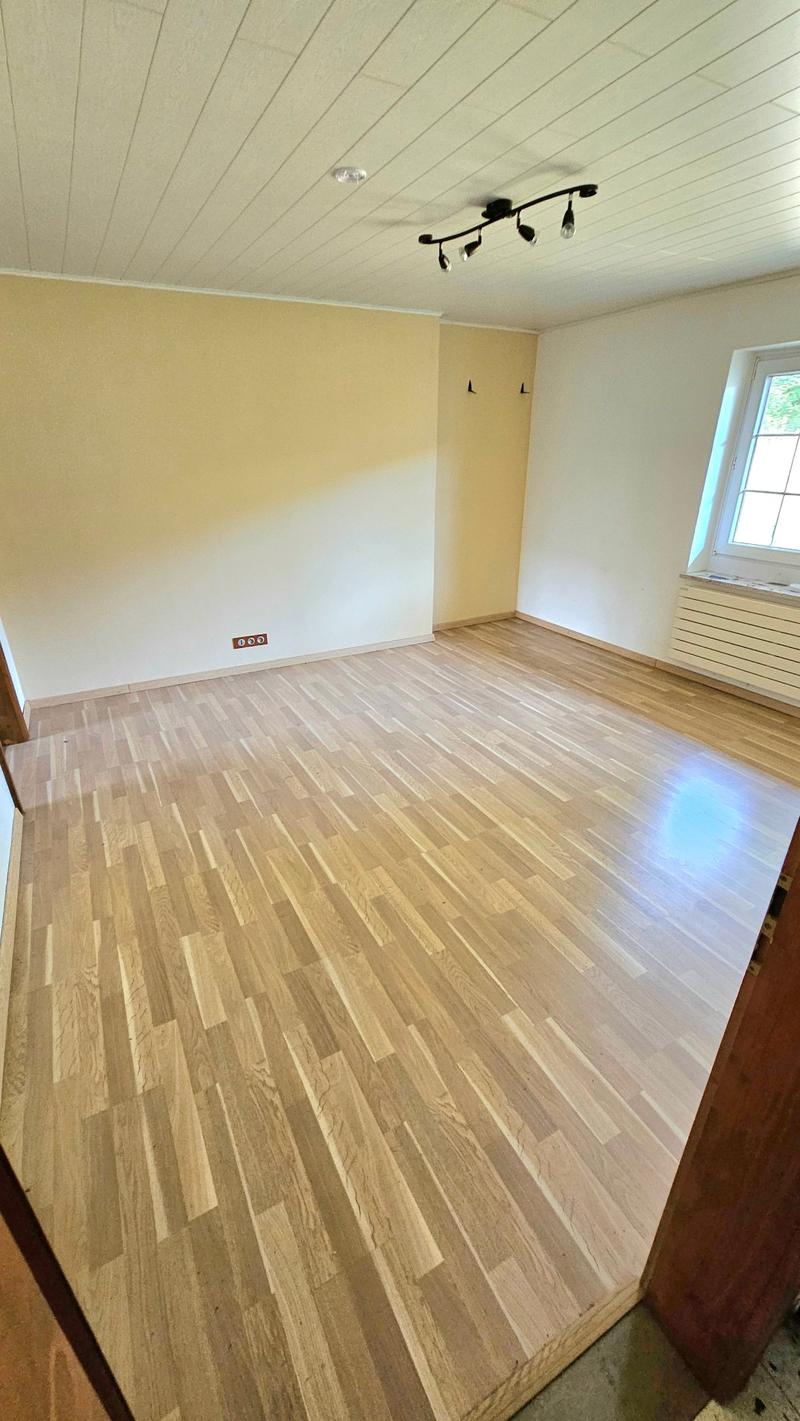 Hardwood floor, white walls, track lighting, electrical outlets, window with wooden frame