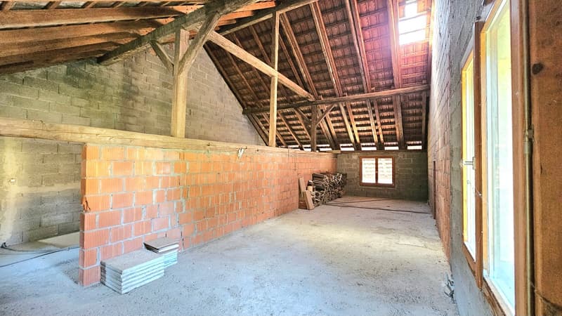 open attic space with wooden trusses, brick walls, glass windows, pile of wood, stack of sheets, unfinished floor