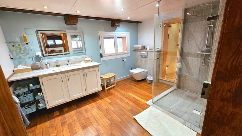 wooden floor, vanity with double sinks, mirror, wooden stool, separate toilet, walk-in shower