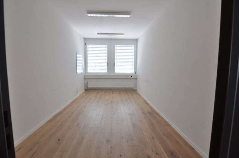 Empty room with white walls, wooden floor, two windows with white blinds, white radiator below the windows