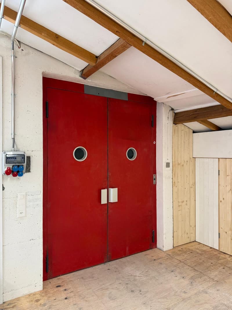 Large red doors with small round windows, concrete walls, wooden ceiling