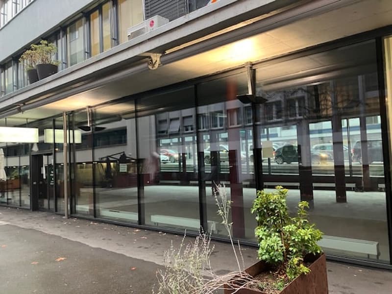 Facade with large glass windows, glass doors, metal railings, and potted plants