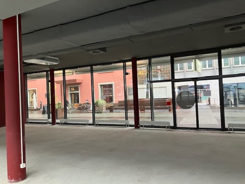empty room with large windows, large red pillars, benches, metal doors, grey flooring