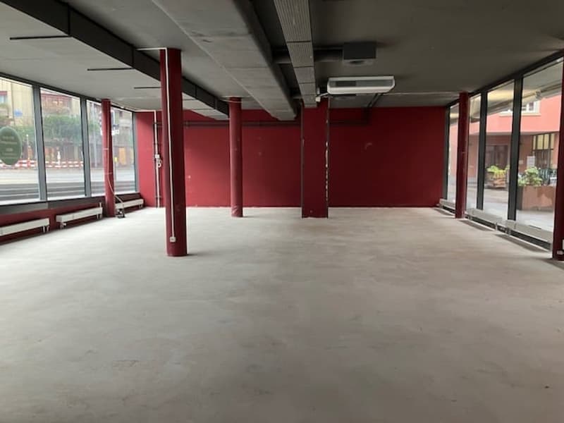 empty building with red painted walls, large windows, concrete floor, central pillars, large openings in walls