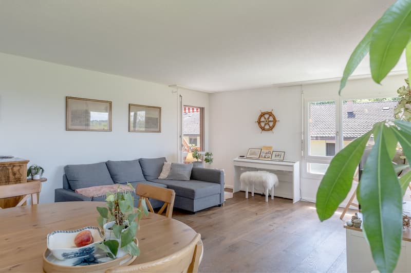 Spacious living room with hardwood floors, gray sofa, wooden coffee table, wall decor, and a large window with a view