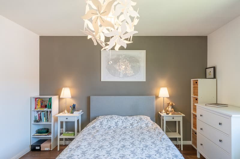 Bedroom with gray walls, white bedding, nightstands, bookshelf, and a decorative light fixture above the bed.