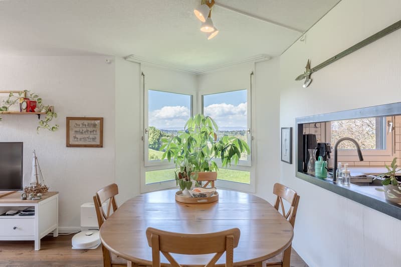 round wooden table, chairs, picture frames on wall, large windows, plant, coffee table, view of outside, sink, faucet, cabinet, countertop