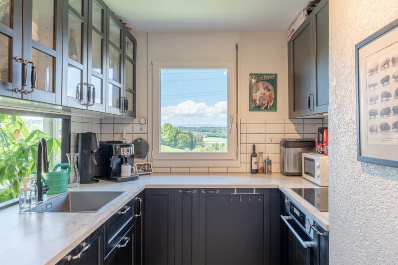 Spacious kitchen with large window offering a scenic view, dark cabinets, stainless steel appliances, and a countertop with various kitchen accessories and decor