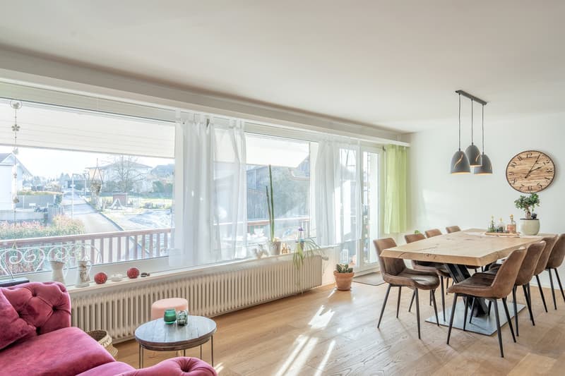 dining table, chairs, couch, radiator, balcony, hanging lamps, clock, large windows, view of outside