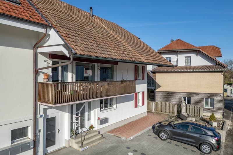 2 story house, white and brown rooftop, white walls, brown balcony, garden, car parked