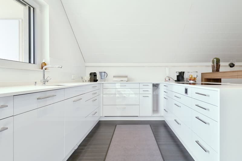 white cabinets, gray flooring, kitchen sink with faucet, built-in coffee machine, countertop with stovetop, basket, glass, cup, bowl
