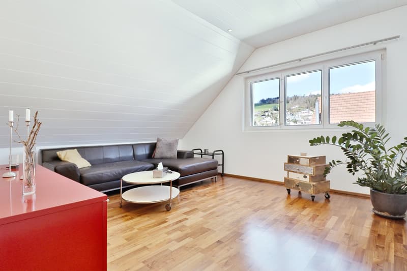 A living room with hardwood floor, white walls, a sofa, coffee table, large window, and view of the outside.