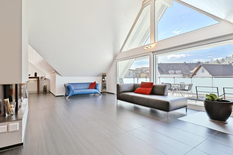 spacious attic room with two couches, fireplace, sliding glass walls, glass table, chairs, and a balcony
