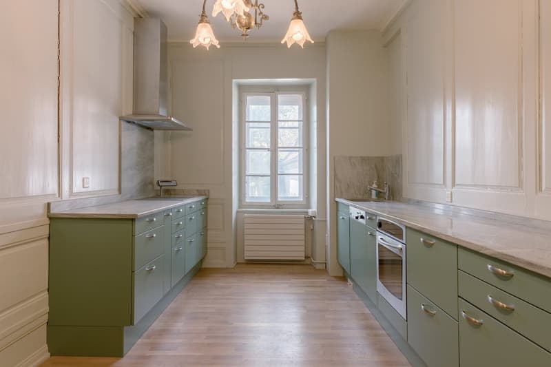 kitchen with green cabinets, marble countertops, white walls, wooden floor, window, chandelier, built-in oven, sink, and faucet