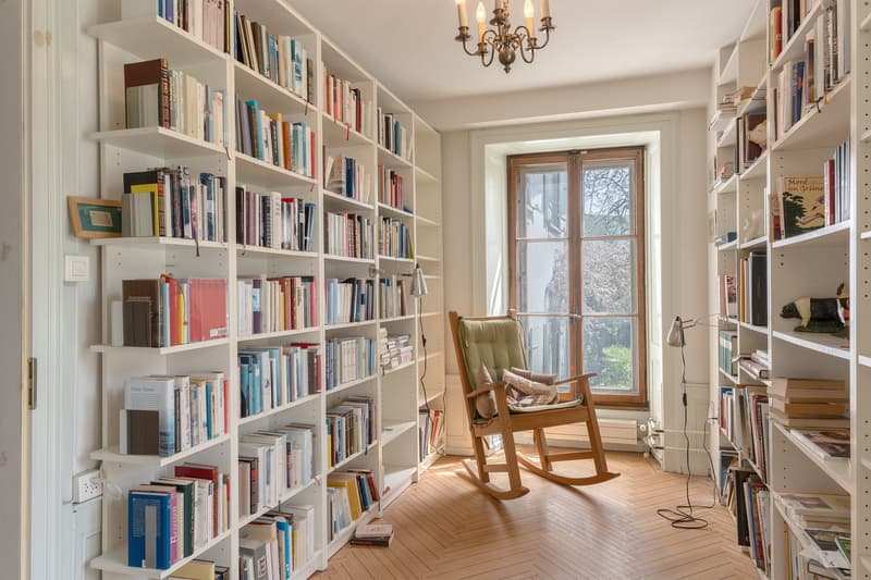 wooden rocking chair, white bookshelves, wooden floor, large window, chandelier