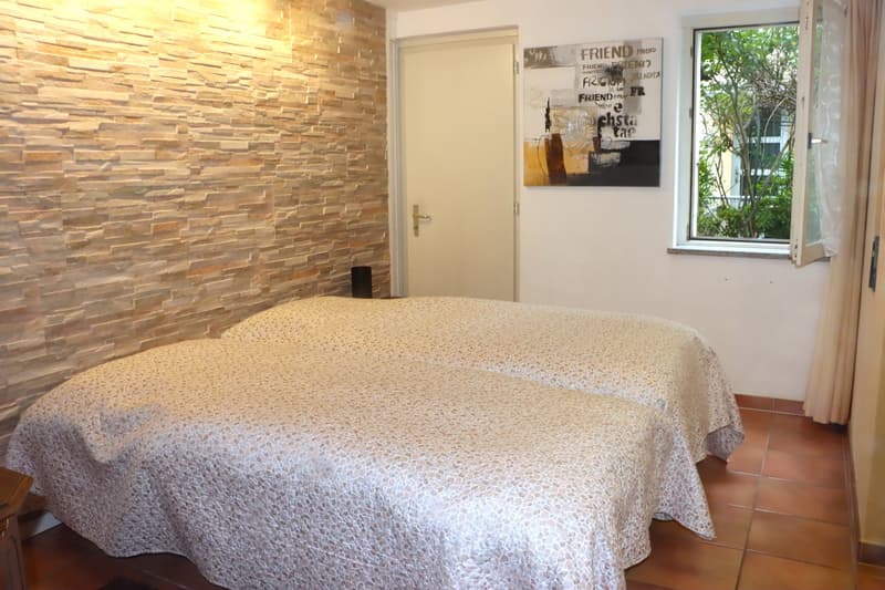 Two twin beds, brick wall, beige comforter, tile floor, speaker, white door, window with outdoor view