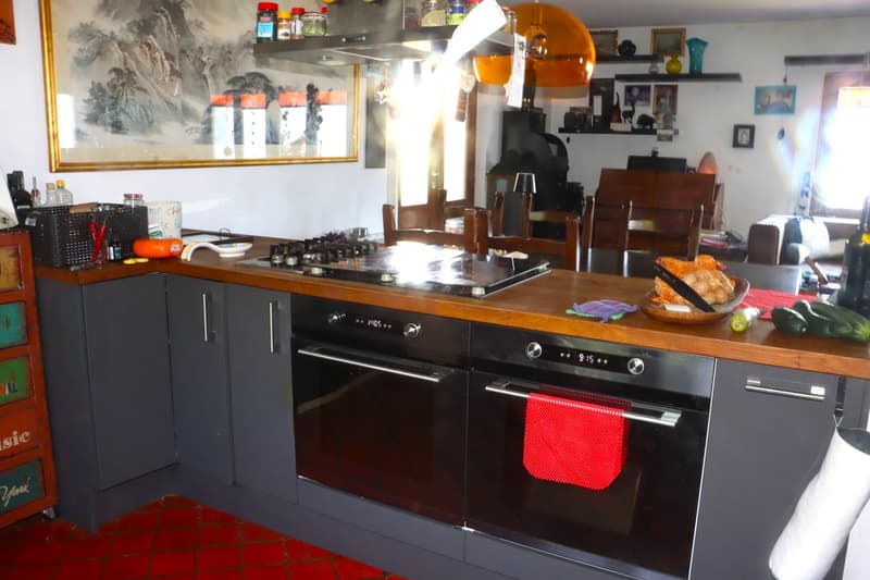 Gas stove, oven, wooden countertops, built-in cabinets, shelves with jars, painting, dining area, couch, lamp