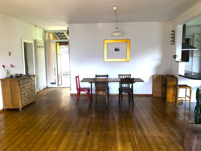 Dining room with wooden floor, white walls, wooden table and chairs, wooden cabinet, flower vase, picture frame, and a lamp