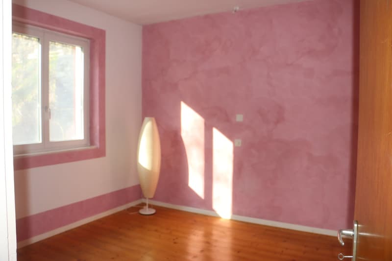 Empty room with wooden floor, pink walls, window, and a lamp