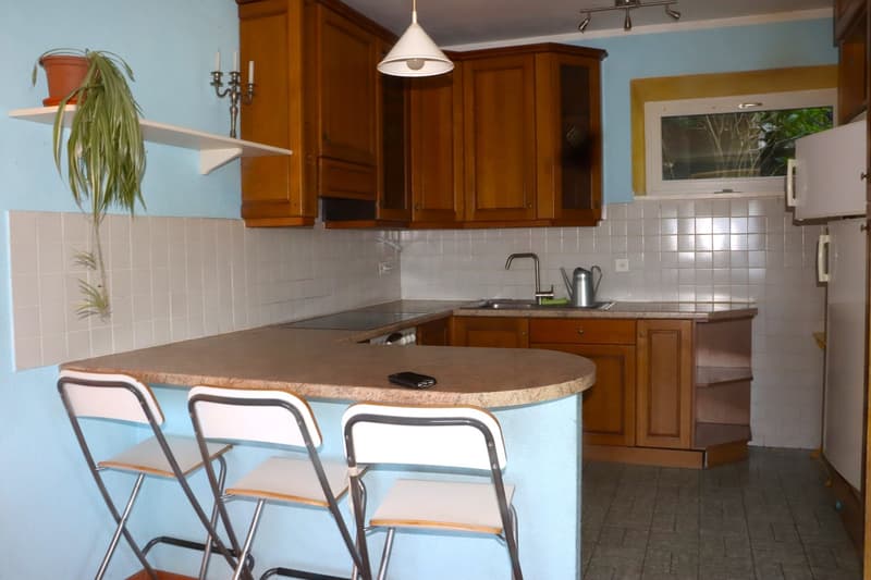 wooden cabinets, tiled walls, countertop, sink, faucet, stove, hanging lamp, potted plant, folding chairs