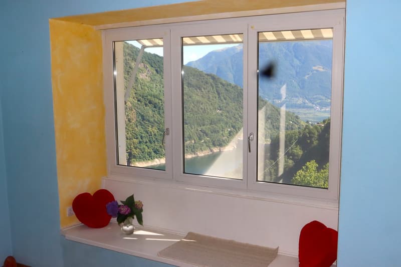 window with view of mountains and river, red heart shaped pillows, flowers in vase