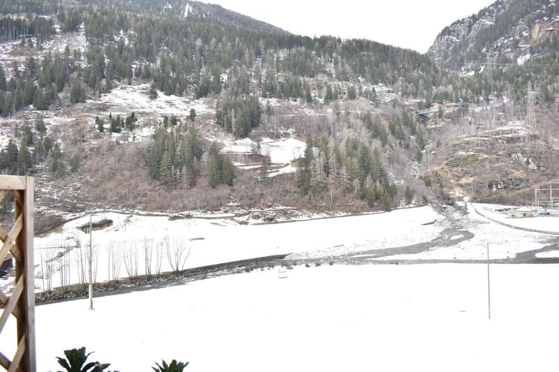 A snowy valley with a river, trees, and mountains in the background