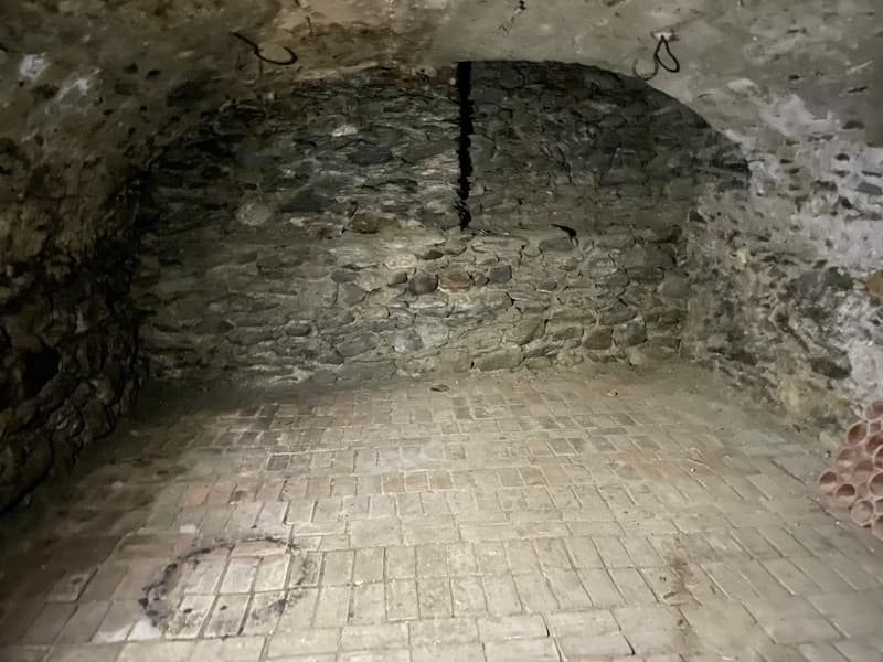 Room with brick flooring, stone walls, arch entrance, stains on the floor