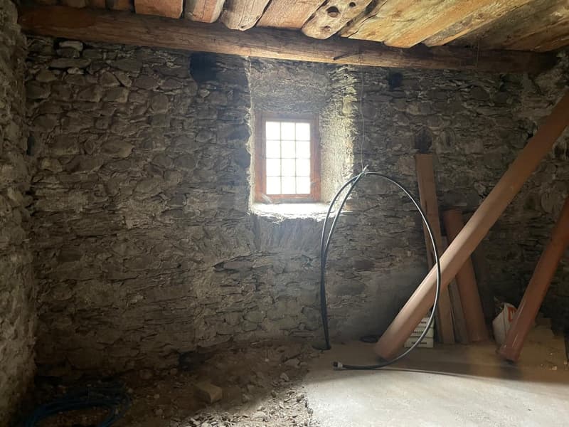 stone walls, small window, wooden beams, wires and pipes on the floor